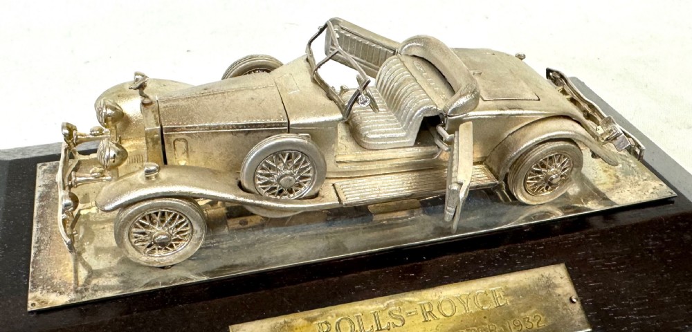 A solid silver model of a classic Rolls Royce Phantom II roadster mounted on a dark wooden plinth inside a presentation box. View XIII