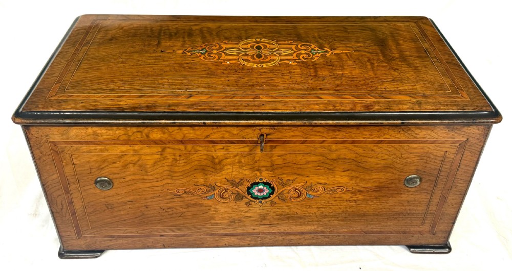 A rectangular rosewood music box featuring floral marquetry inlays on the lid and front panel, flanked by ebonised borders with a key inserted. View II
