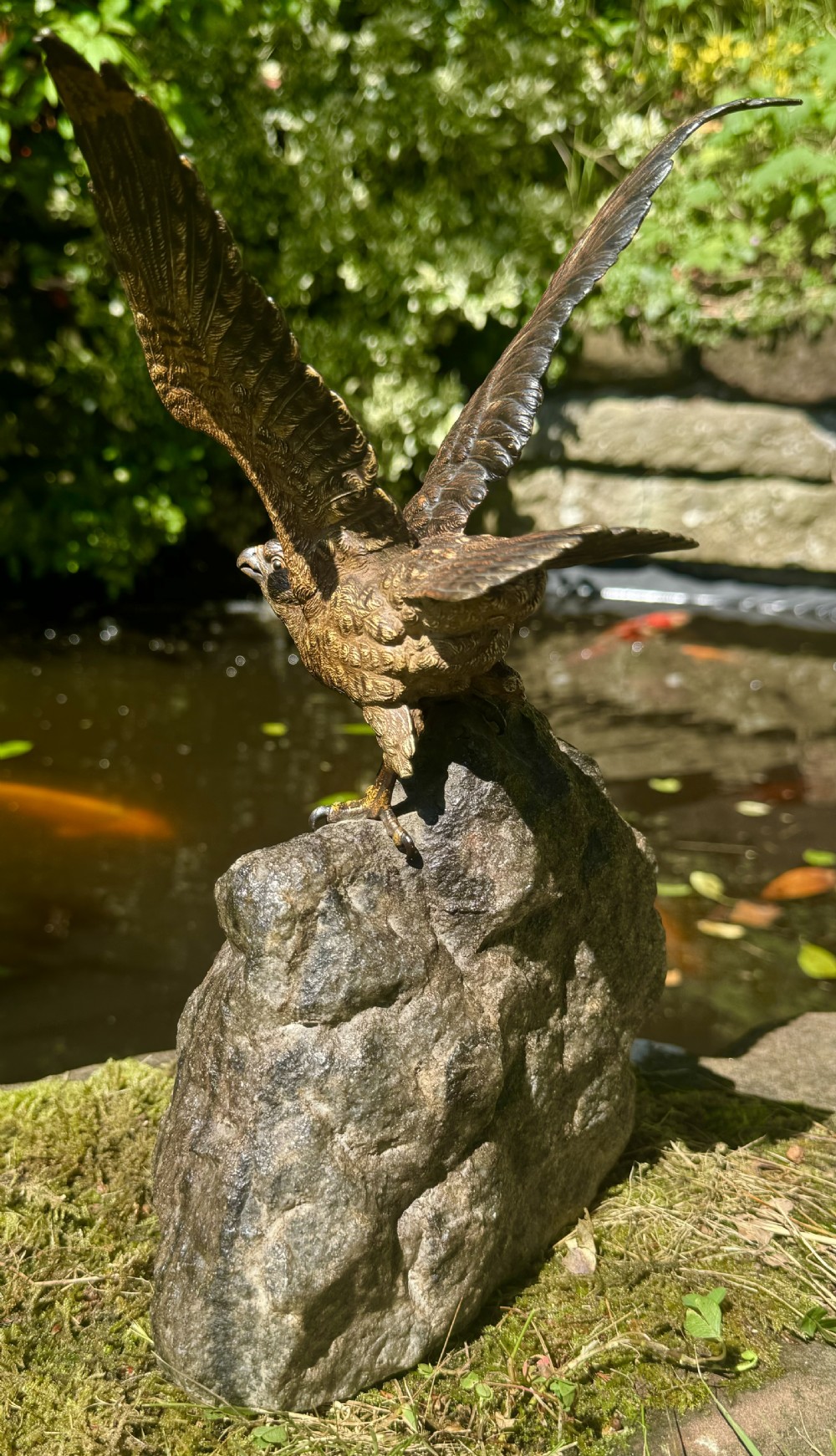 A cold-painted bronze sculpture depicting a hawk with open wings perched atop a natural quartz stone base. View X