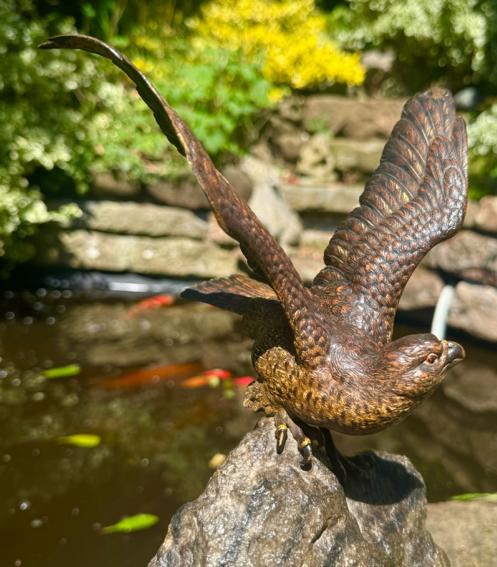A cold-painted bronze sculpture depicting a hawk with open wings perched atop a natural quartz stone base. View XVI