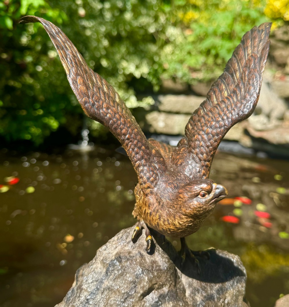 A cold-painted bronze sculpture depicting a hawk with open wings perched atop a natural quartz stone base. View XVII