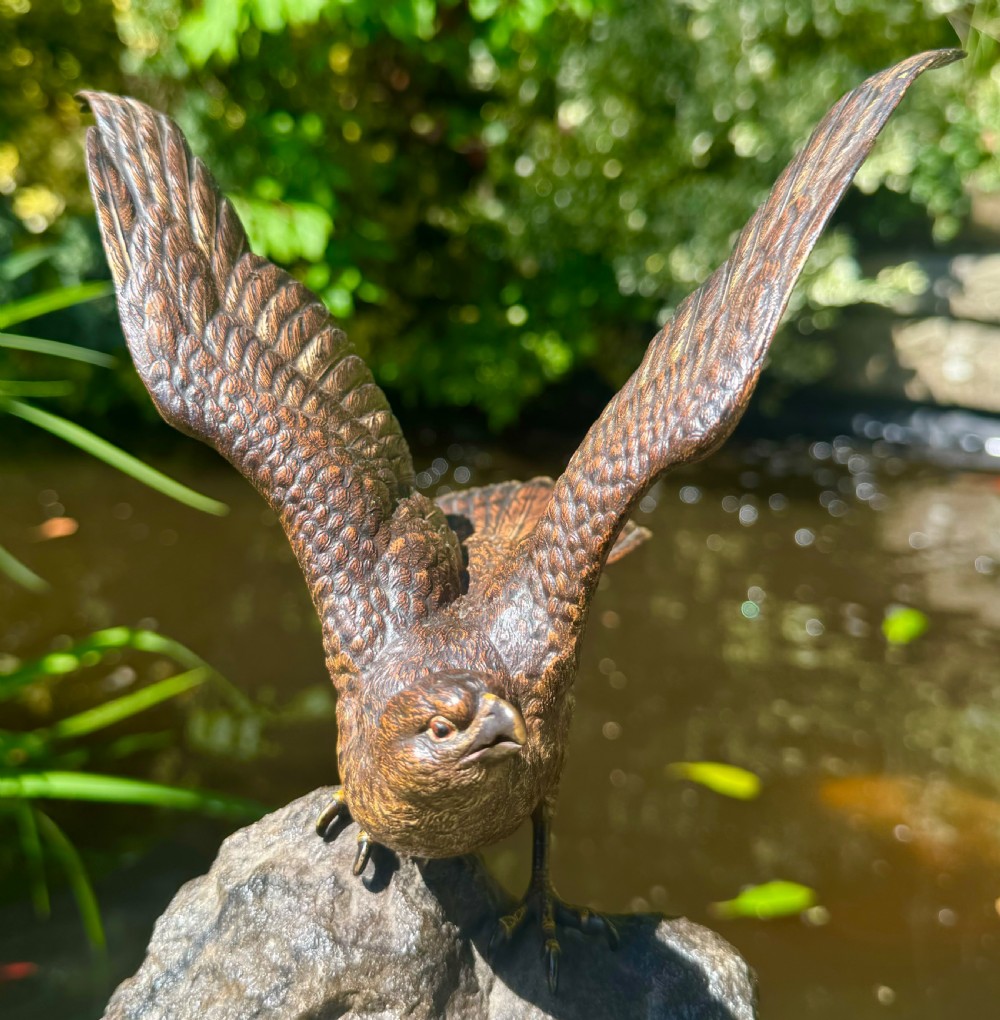 A cold-painted bronze sculpture depicting a hawk with open wings perched atop a natural quartz stone base. View XXII