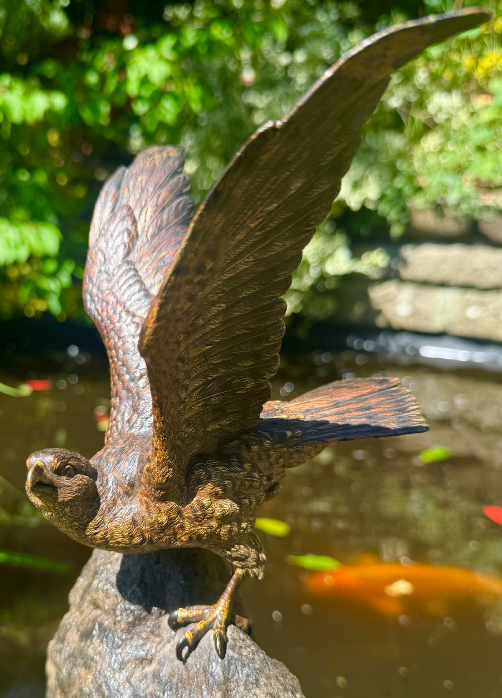 A cold-painted bronze sculpture depicting a hawk with open wings perched atop a natural quartz stone base. View XXIV
