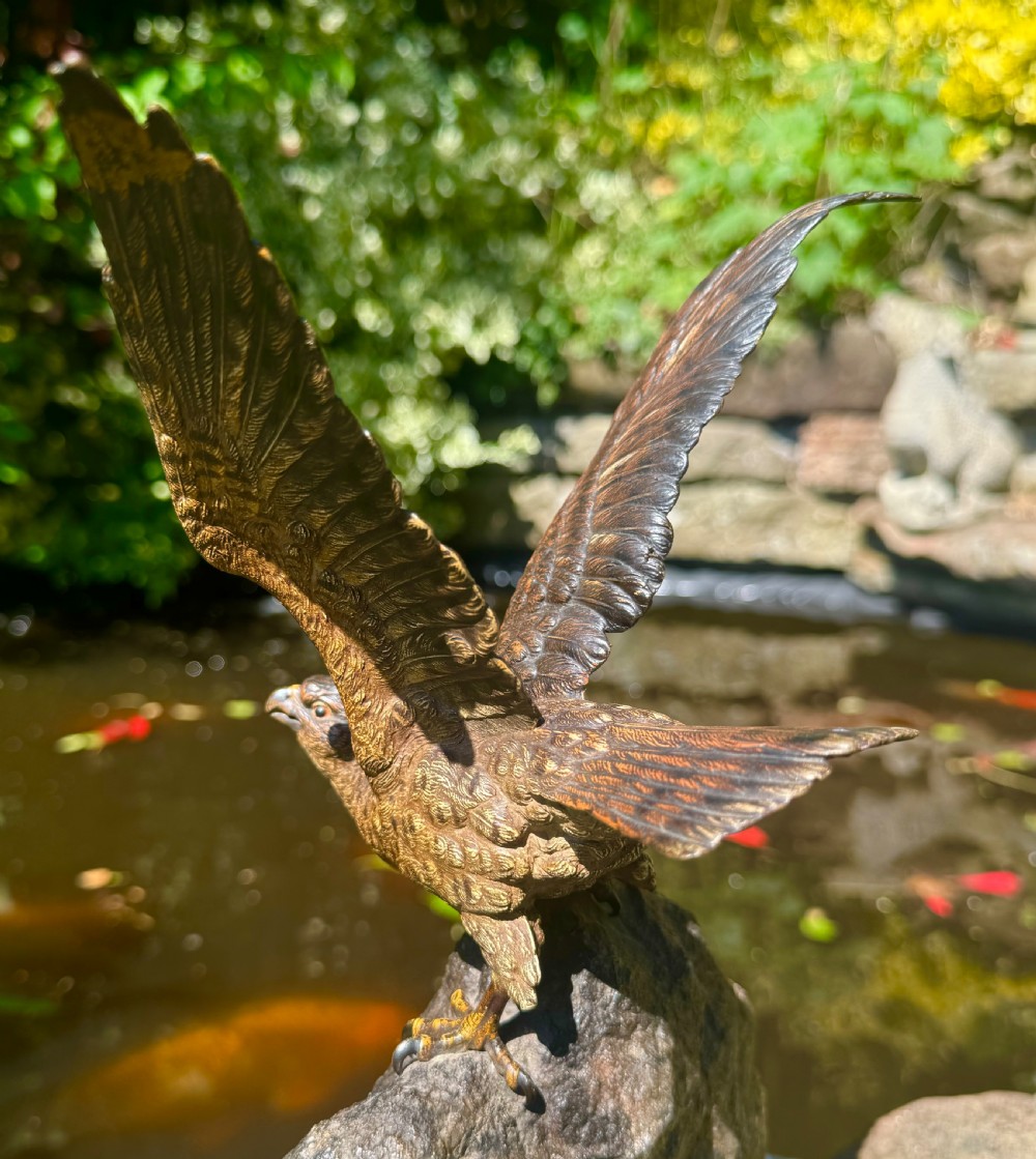 A cold-painted bronze sculpture depicting a hawk with open wings perched atop a natural quartz stone base. View XXVI