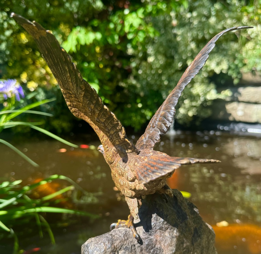 A cold-painted bronze sculpture depicting a hawk with open wings perched atop a natural quartz stone base. View XXVII