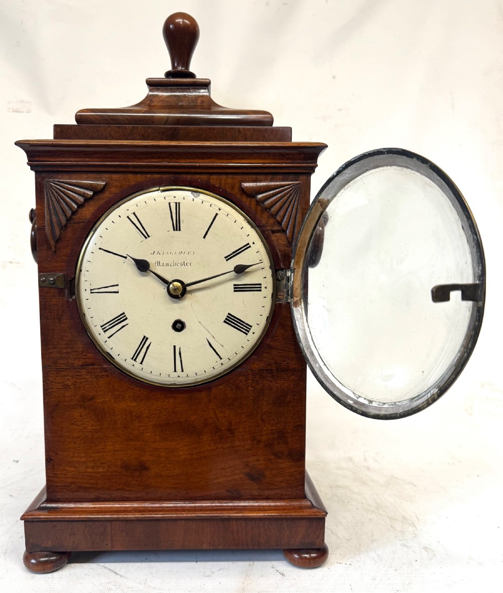 A mahogany single fusee mantel clock featuring a turned finial top, carved fan spandrels, a white dial with Roman numerals signed J Kingerley Manchester, and bun feet. View III