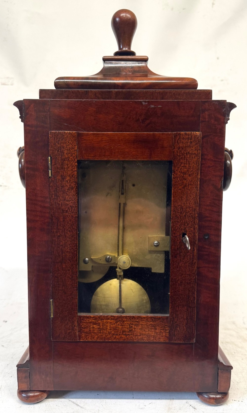 A mahogany single fusee mantel clock featuring a turned finial top, carved fan spandrels, a white dial with Roman numerals signed J Kingerley Manchester, and bun feet. View VII