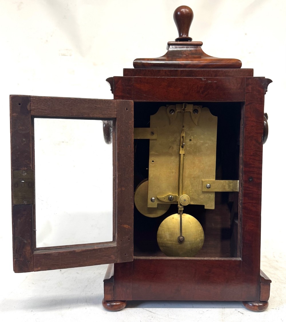 A mahogany single fusee mantel clock featuring a turned finial top, carved fan spandrels, a white dial with Roman numerals signed J Kingerley Manchester, and bun feet. View X