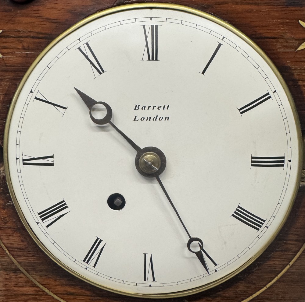 An antique mahogany mantel clock featuring a carved pagoda top, brass inlay details, side ring handles, and a white circular dial signed Barrett London with Roman numerals. View III