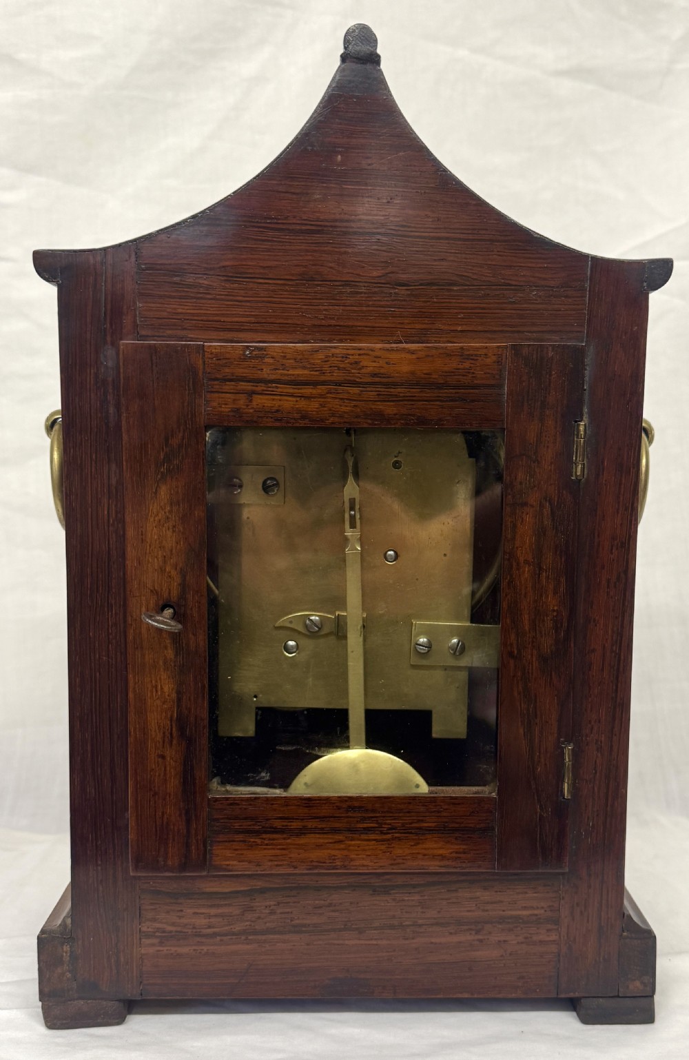 An antique mahogany mantel clock featuring a carved pagoda top, brass inlay details, side ring handles, and a white circular dial signed Barrett London with Roman numerals. View VII