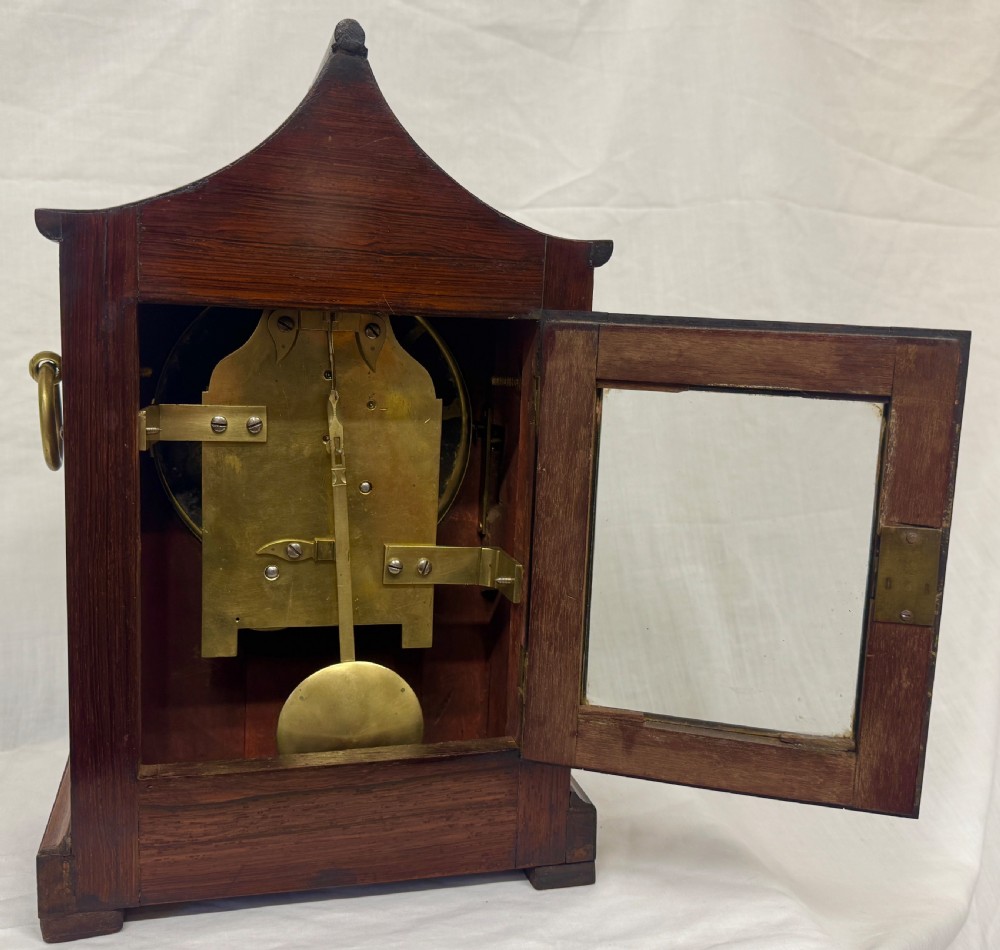 An antique mahogany mantel clock featuring a carved pagoda top, brass inlay details, side ring handles, and a white circular dial signed Barrett London with Roman numerals. View VIII