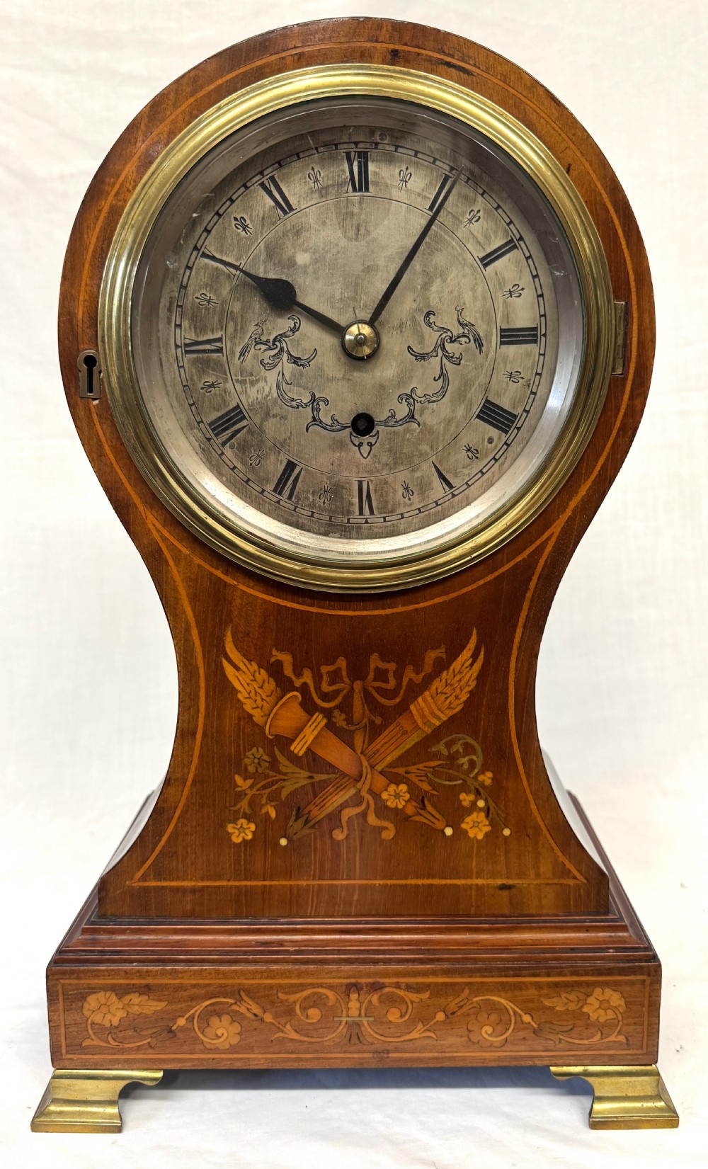 An antique balloon-shaped mahogany mantel clock featuring marquetry inlay, a silvered dial with Roman numerals, and brass bracket feet. View II