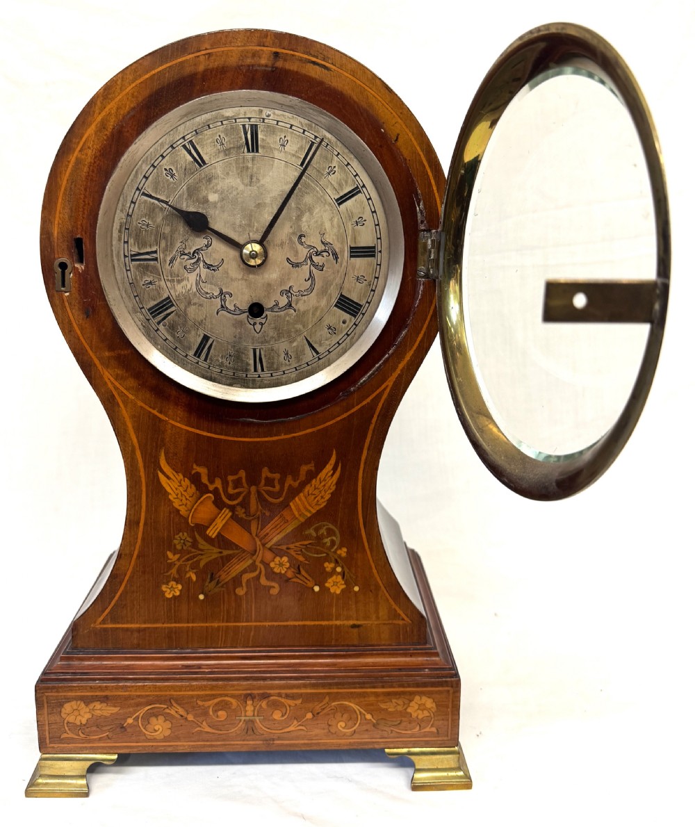 An antique balloon-shaped mahogany mantel clock featuring marquetry inlay, a silvered dial with Roman numerals, and brass bracket feet. View III