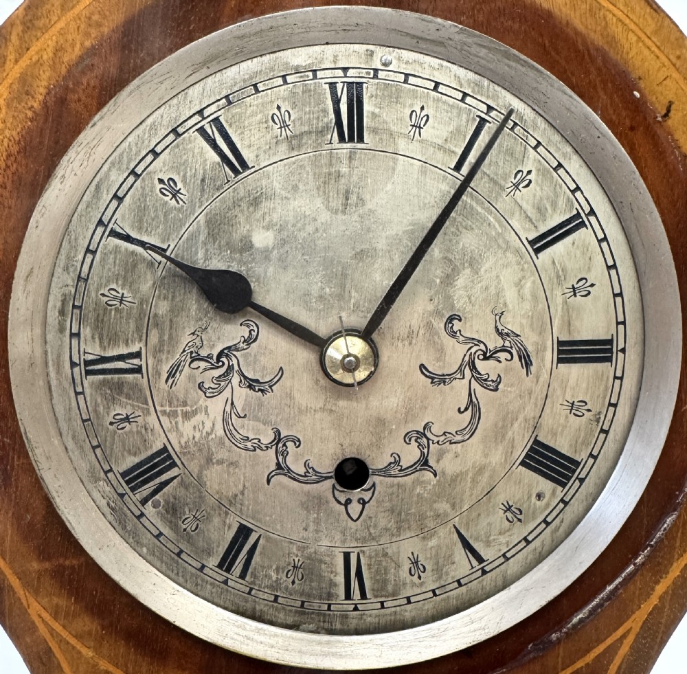 An antique balloon-shaped mahogany mantel clock featuring marquetry inlay, a silvered dial with Roman numerals, and brass bracket feet. View IV