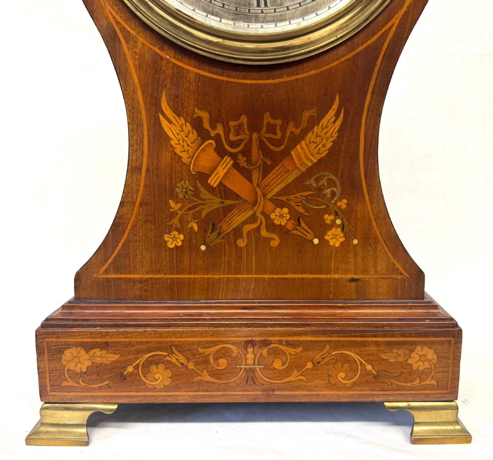 An antique balloon-shaped mahogany mantel clock featuring marquetry inlay, a silvered dial with Roman numerals, and brass bracket feet. View V