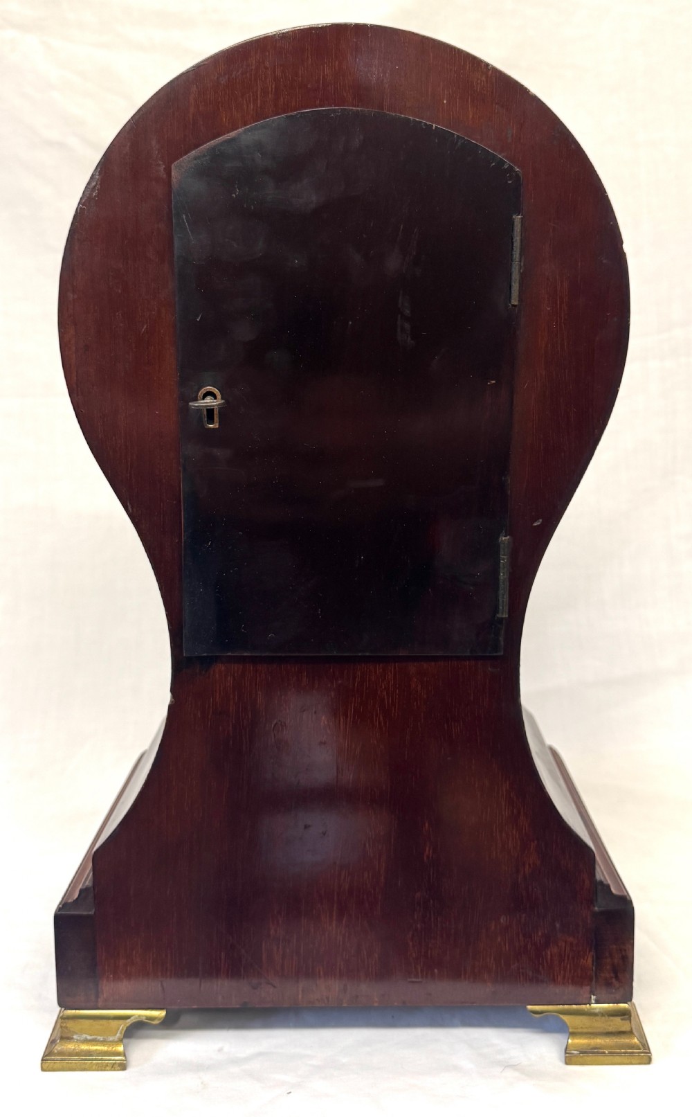 An antique balloon-shaped mahogany mantel clock featuring marquetry inlay, a silvered dial with Roman numerals, and brass bracket feet. View VIII