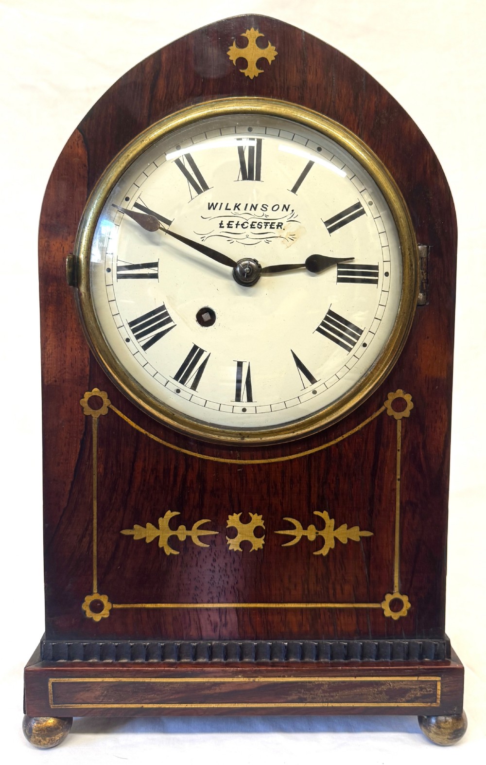 A dark mahogany lancet top mantel clock featuring brass inlay motifs, a circular white dial with Roman numerals, side ring handles, and brass ball feet. View II