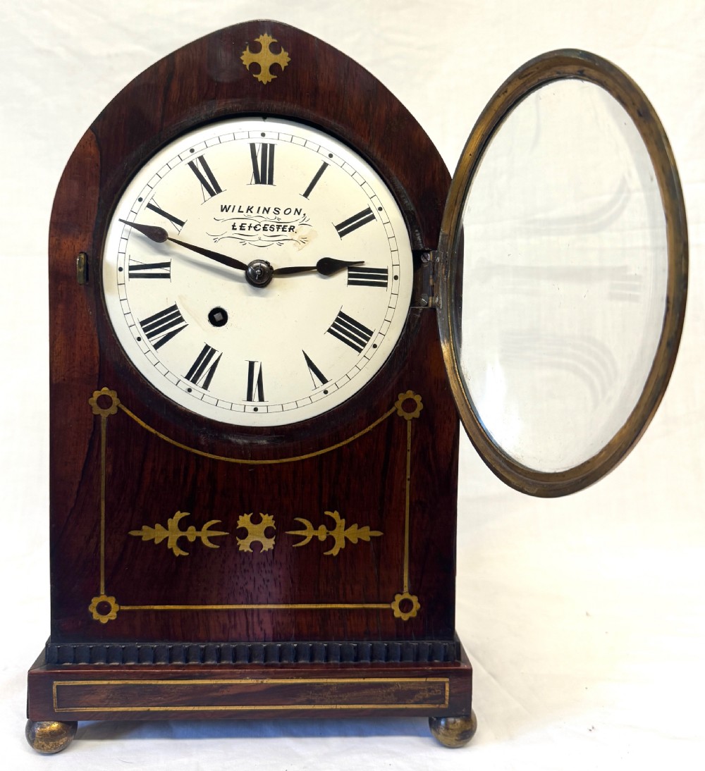 A dark mahogany lancet top mantel clock featuring brass inlay motifs, a circular white dial with Roman numerals, side ring handles, and brass ball feet. View III