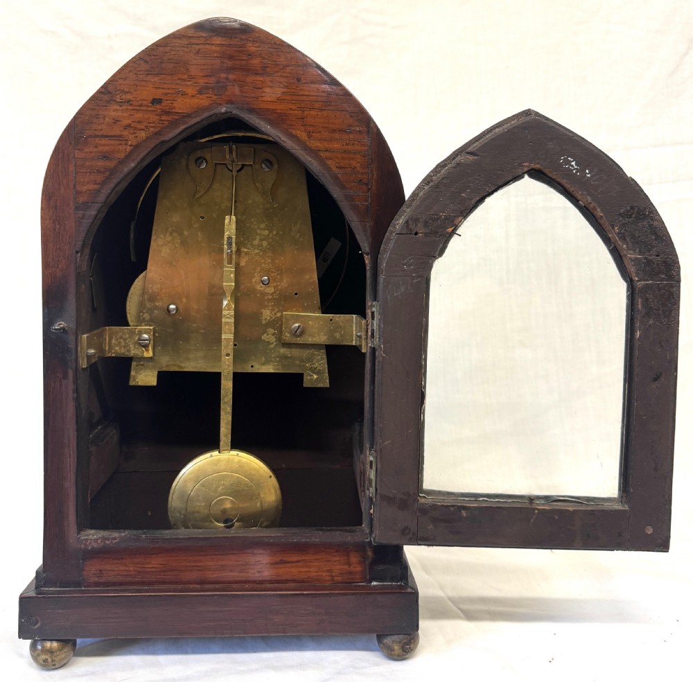 A dark mahogany lancet top mantel clock featuring brass inlay motifs, a circular white dial with Roman numerals, side ring handles, and brass ball feet. View VIII