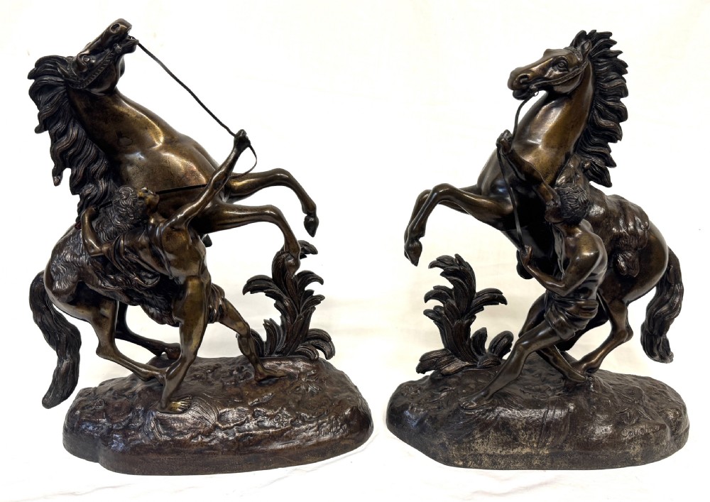A pair of dark patinated bronze equestrian sculptures depicting rearing horses restrained by grooms on naturalistic rockwork bases. View II