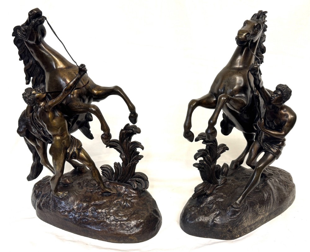 A pair of dark patinated bronze equestrian sculptures depicting rearing horses restrained by grooms on naturalistic rockwork bases. View III
