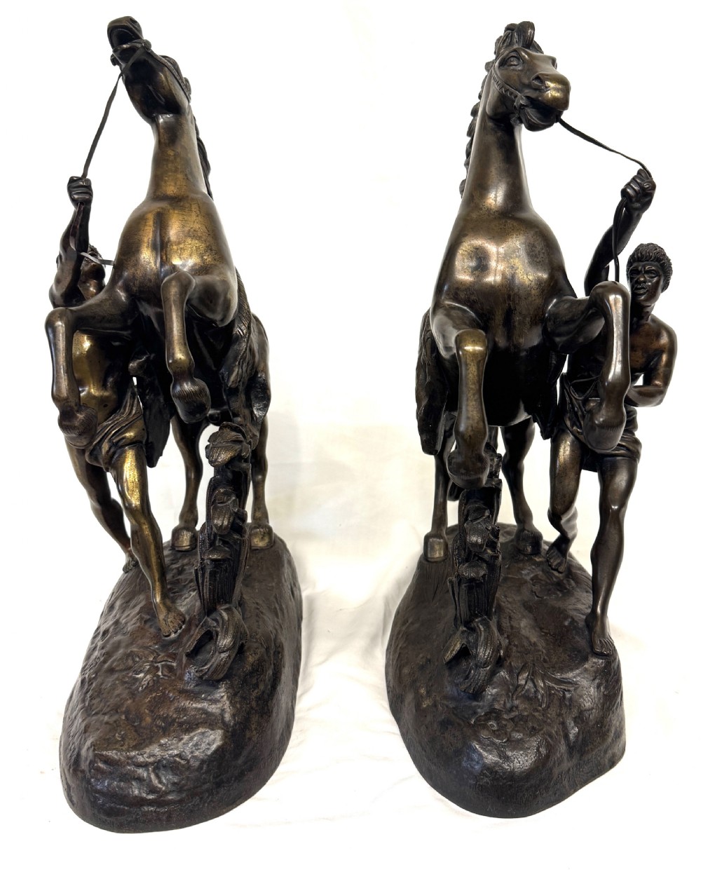 A pair of dark patinated bronze equestrian sculptures depicting rearing horses restrained by grooms on naturalistic rockwork bases. View IV