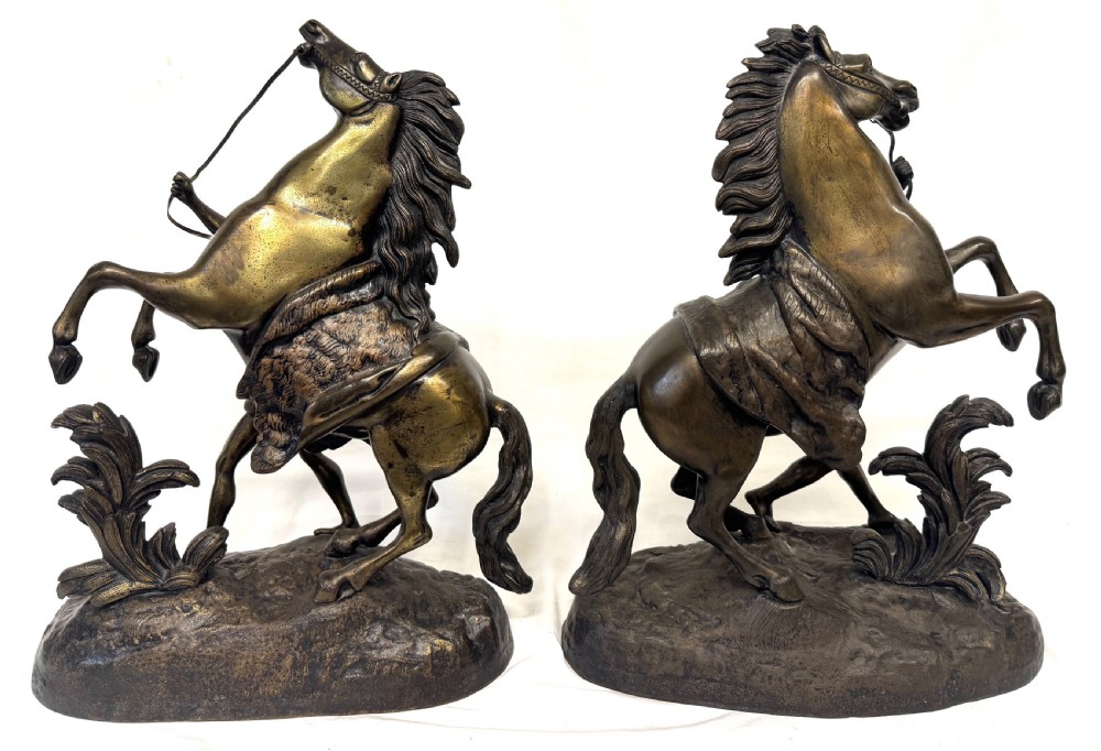 A pair of dark patinated bronze equestrian sculptures depicting rearing horses restrained by grooms on naturalistic rockwork bases. View V