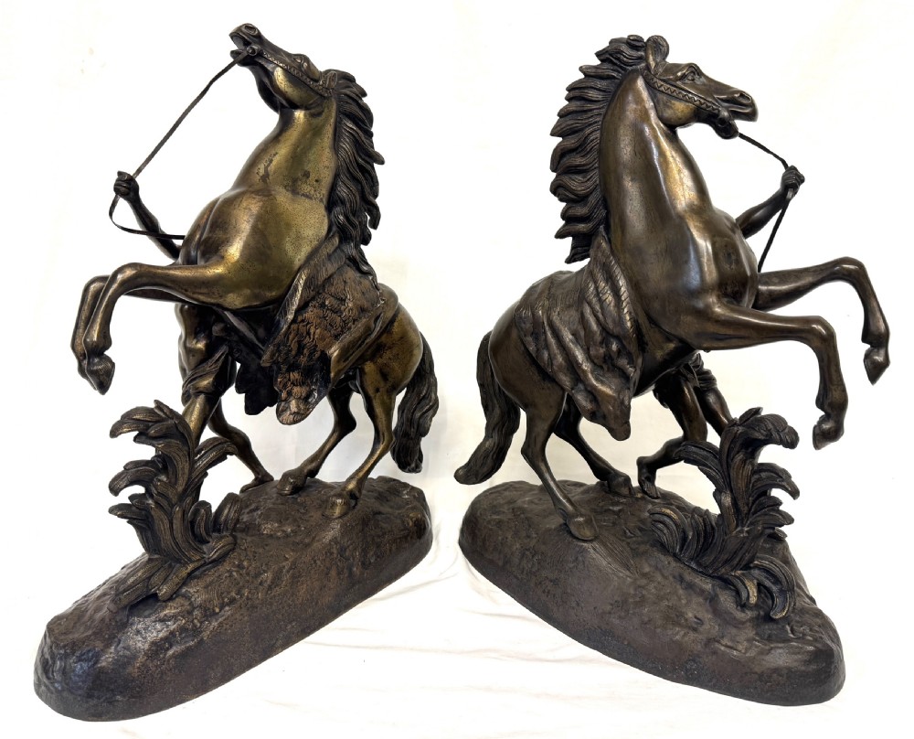 A pair of dark patinated bronze equestrian sculptures depicting rearing horses restrained by grooms on naturalistic rockwork bases. View VI