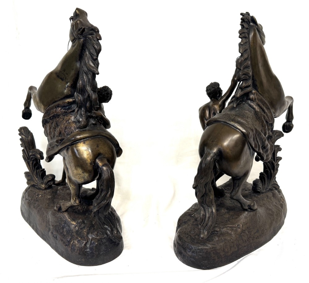 A pair of dark patinated bronze equestrian sculptures depicting rearing horses restrained by grooms on naturalistic rockwork bases. View VII