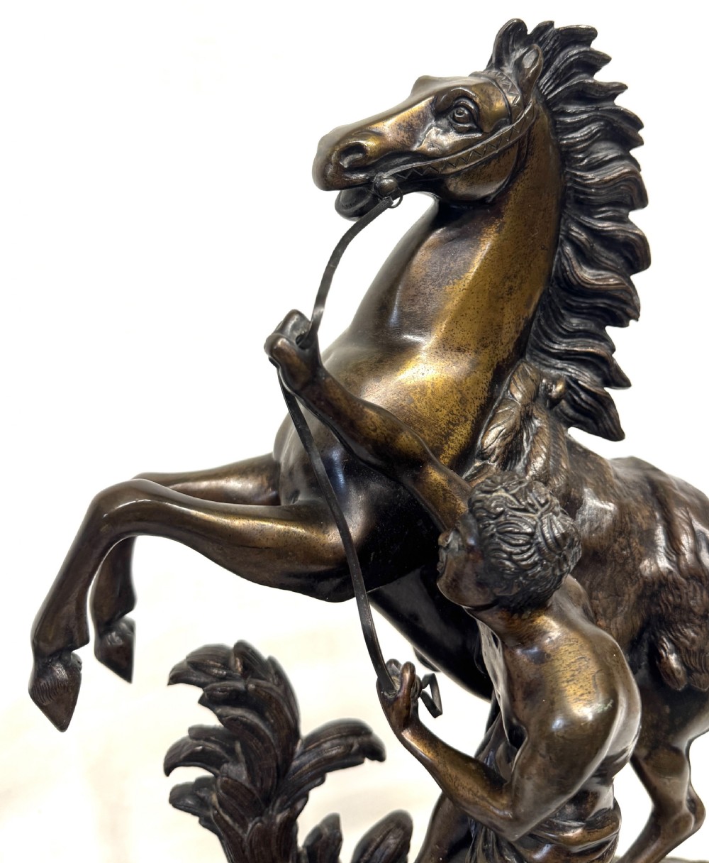 A pair of dark patinated bronze equestrian sculptures depicting rearing horses restrained by grooms on naturalistic rockwork bases. View X