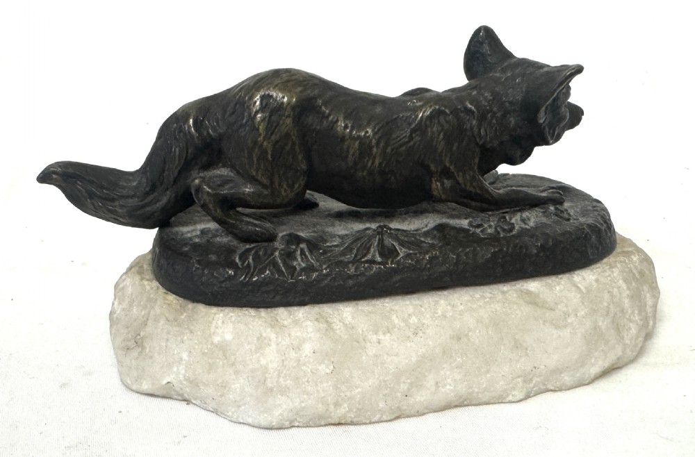 An antique dark bronze sculpture of a prowling fox set upon a naturalistic metal mound atop a cream marble base. View VI