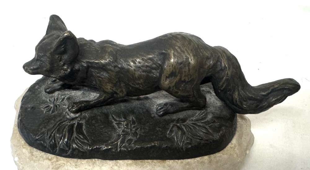 An antique dark bronze sculpture of a prowling fox set upon a naturalistic metal mound atop a cream marble base. View X