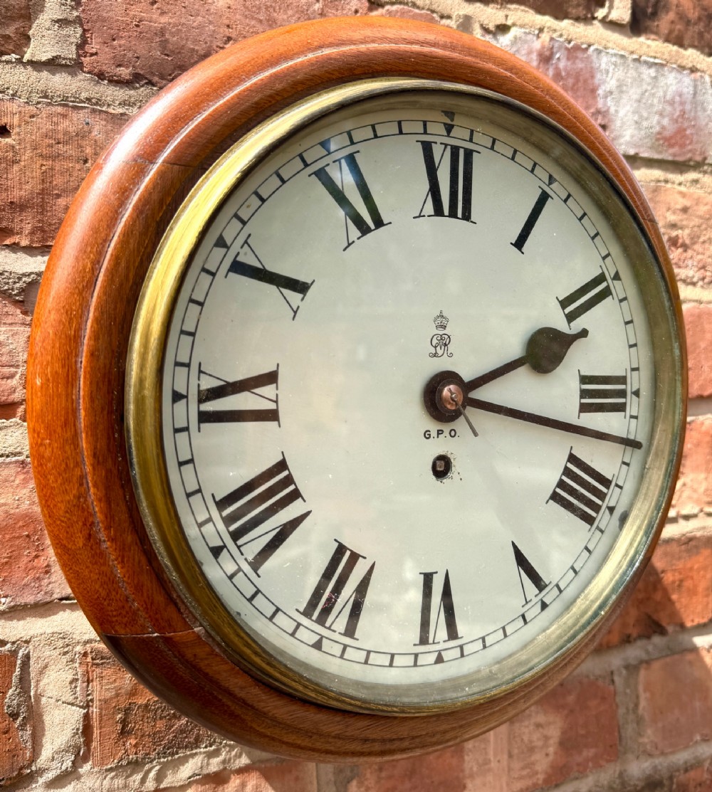 A circular antique mahogany wall clock with a brass bezel and an off-white dial marked with Roman numerals and the GPO stamp.