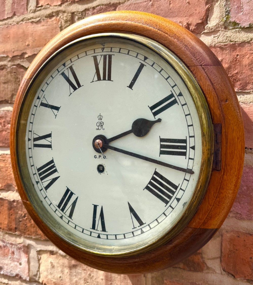 A circular antique mahogany wall clock with a brass bezel and an off-white dial marked with Roman numerals and the GPO stamp. View II