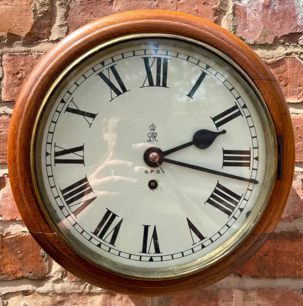 A circular antique mahogany wall clock with a brass bezel and an off-white dial marked with Roman numerals and the GPO stamp. View III