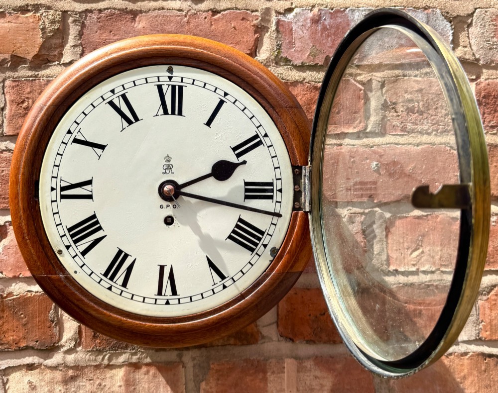 A circular antique mahogany wall clock with a brass bezel and an off-white dial marked with Roman numerals and the GPO stamp. View IV