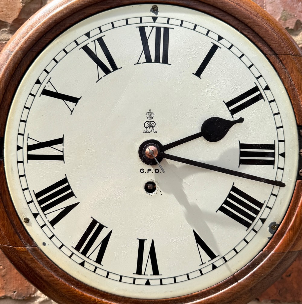 A circular antique mahogany wall clock with a brass bezel and an off-white dial marked with Roman numerals and the GPO stamp. View V