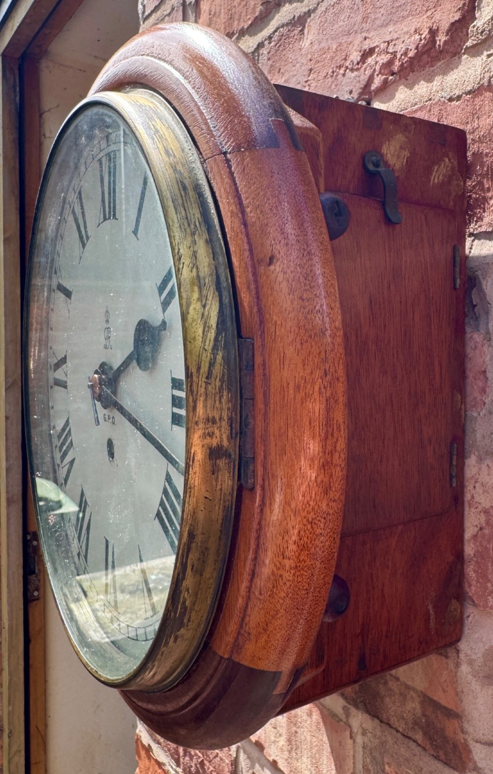 A circular antique mahogany wall clock with a brass bezel and an off-white dial marked with Roman numerals and the GPO stamp. View VIII