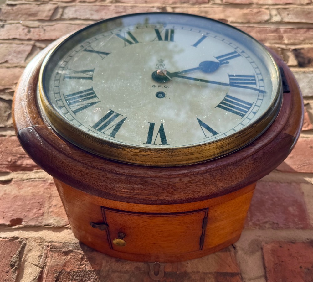 A circular antique mahogany wall clock with a brass bezel and an off-white dial marked with Roman numerals and the GPO stamp. View IX