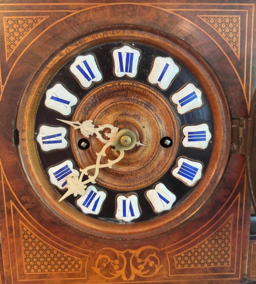 An antique walnut and ebonised cuckoo mantel clock featuring floral marquetry inlays, an architectural domed pediment, and an enamel cartouche dial. View V