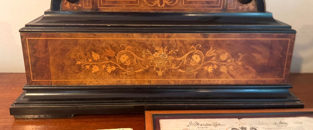An antique walnut and ebonised cuckoo mantel clock featuring floral marquetry inlays, an architectural domed pediment, and an enamel cartouche dial. View VI