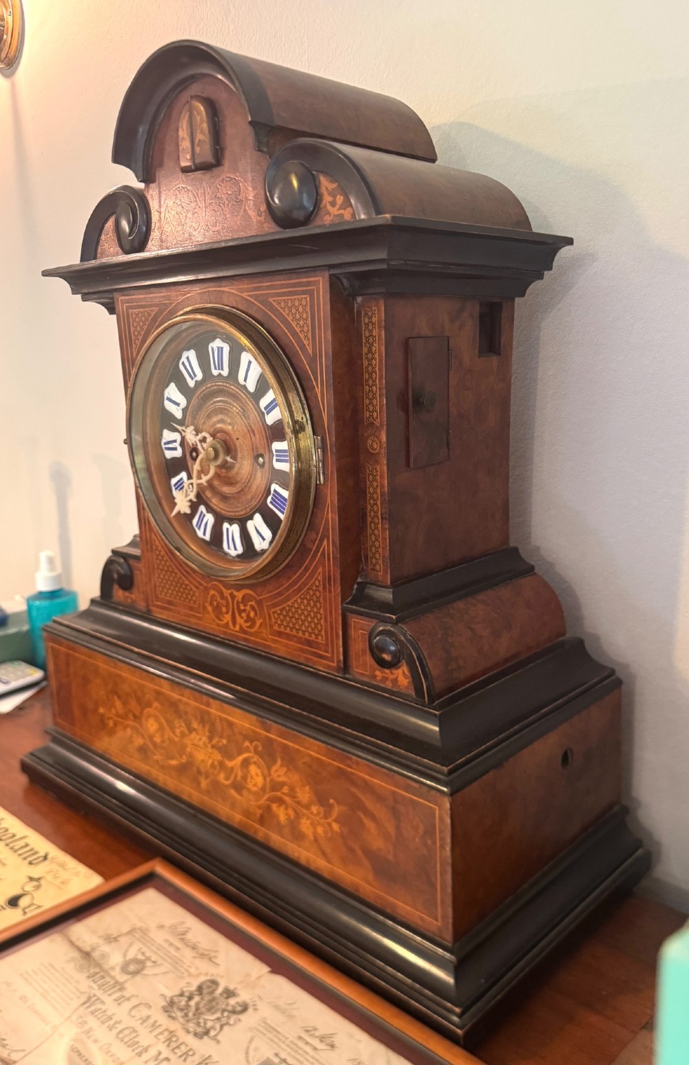 An antique walnut and ebonised cuckoo mantel clock featuring floral marquetry inlays, an architectural domed pediment, and an enamel cartouche dial. View VIII