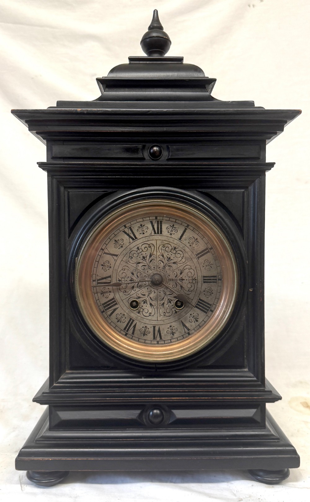 An ebonised wooden mantel clock featuring a stepped pedestal base, turned finial, and an engraved silvered metal dial with Roman numerals. View II
