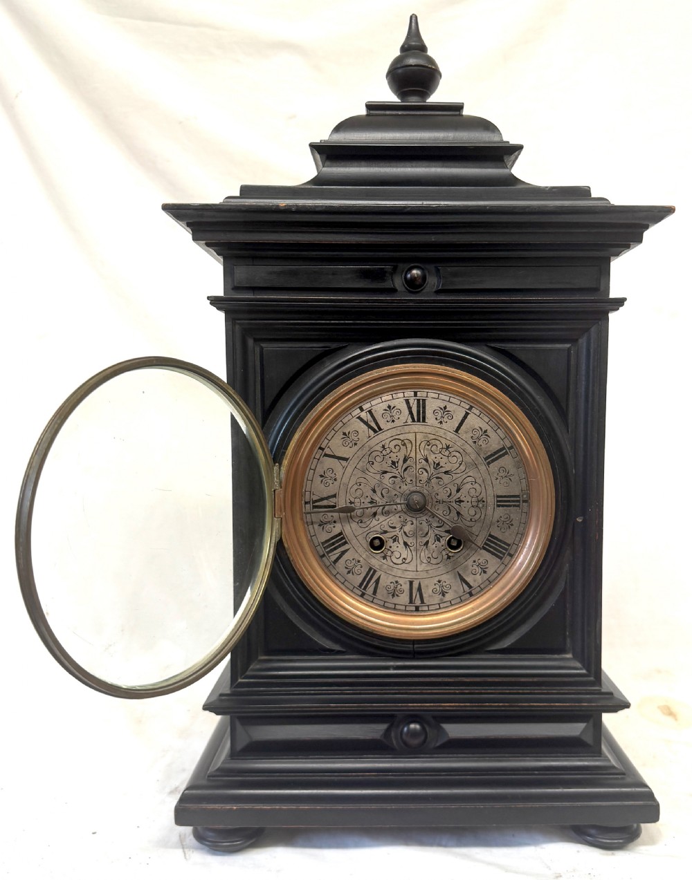 An ebonised wooden mantel clock featuring a stepped pedestal base, turned finial, and an engraved silvered metal dial with Roman numerals. View III