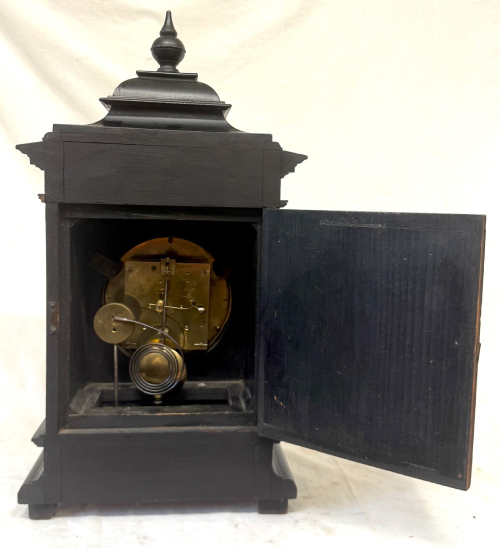 An ebonised wooden mantel clock featuring a stepped pedestal base, turned finial, and an engraved silvered metal dial with Roman numerals. View VIII