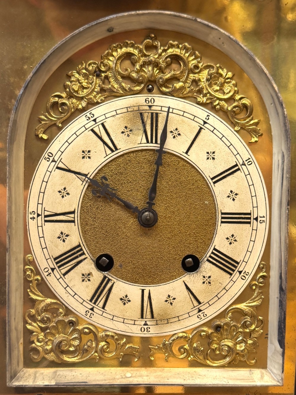An antique walnut bracket clock featuring an arched brass dial with decorative corner spandrels, Roman numerals, and turned finials on a stepped wood base. View IV