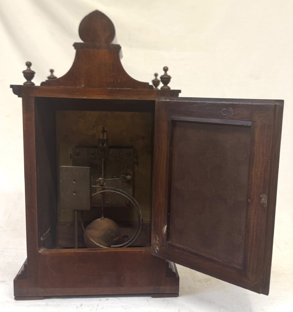 An antique walnut bracket clock featuring an arched brass dial with decorative corner spandrels, Roman numerals, and turned finials on a stepped wood base. View VIII
