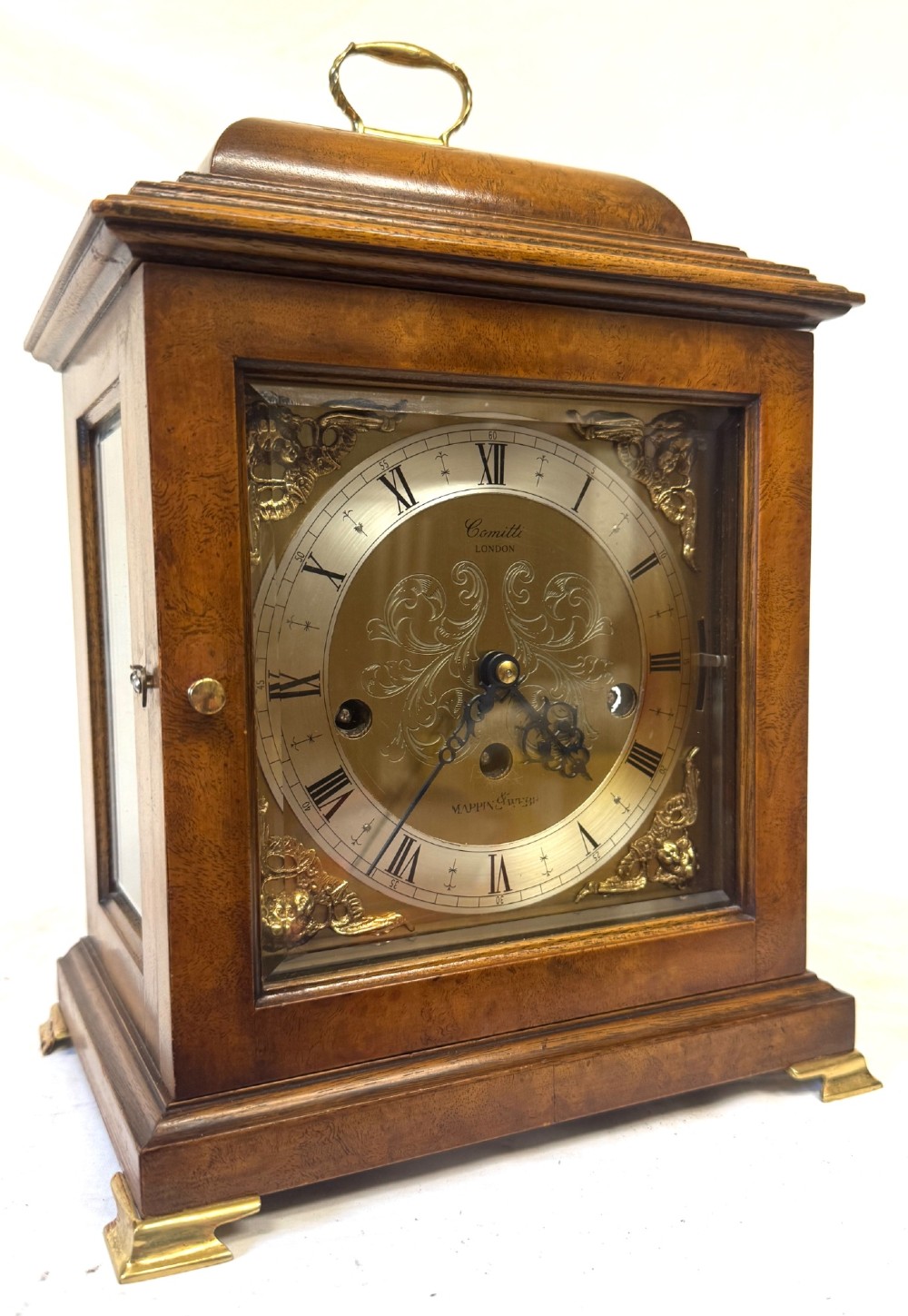 A burr walnut basket top mantel clock featuring an etched brass dial with Roman numerals, corner spandrels, side glass panels, and a top brass handle.