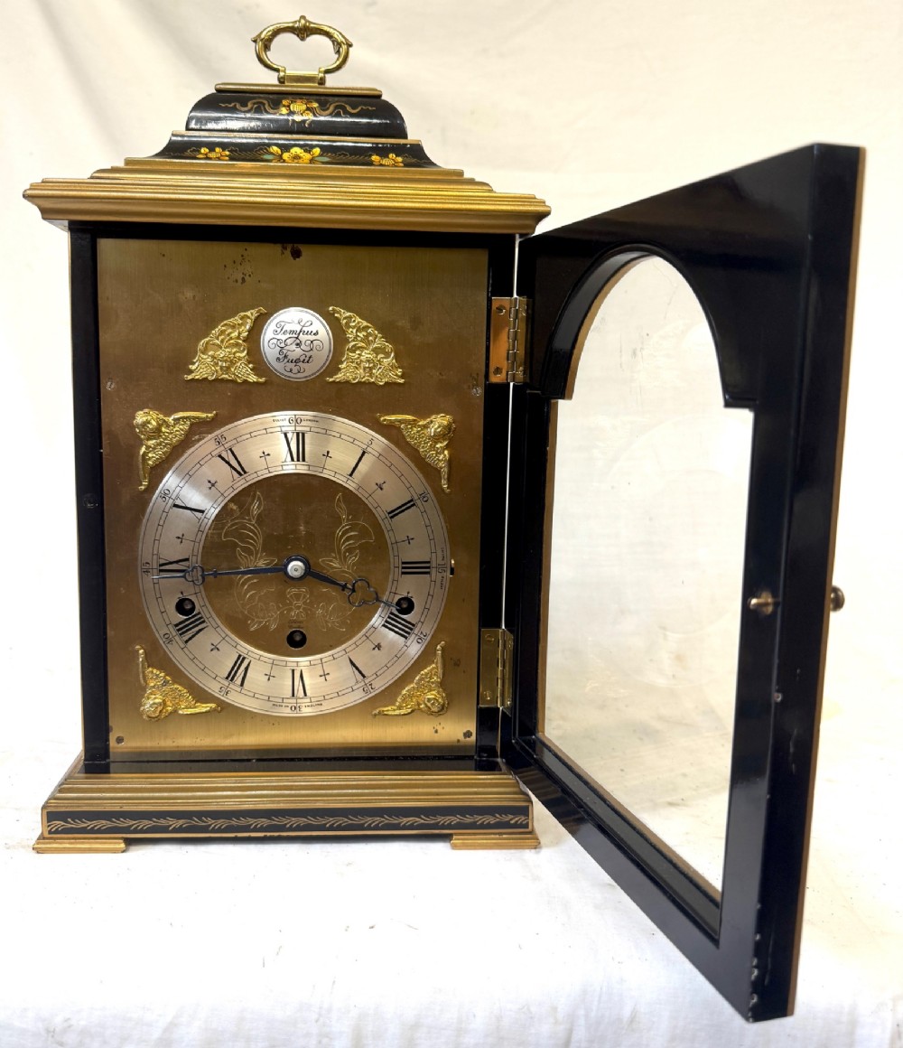 A black lacquered chinoiserie bracket clock featuring hand-painted gilt landscape scenes, a brass dial with Roman numerals, and a top brass carrying handle. View III
