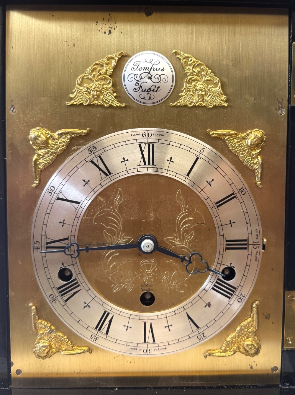 A black lacquered chinoiserie bracket clock featuring hand-painted gilt landscape scenes, a brass dial with Roman numerals, and a top brass carrying handle. View IV